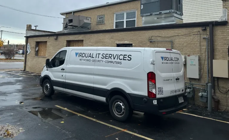 White Virdual IT Services van parked behind a brick commercial building on a wet day